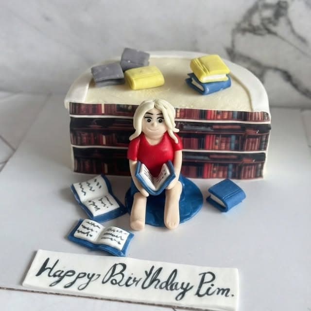 Book-themed birthday cake with shelves, miniature books, and a reader figurine