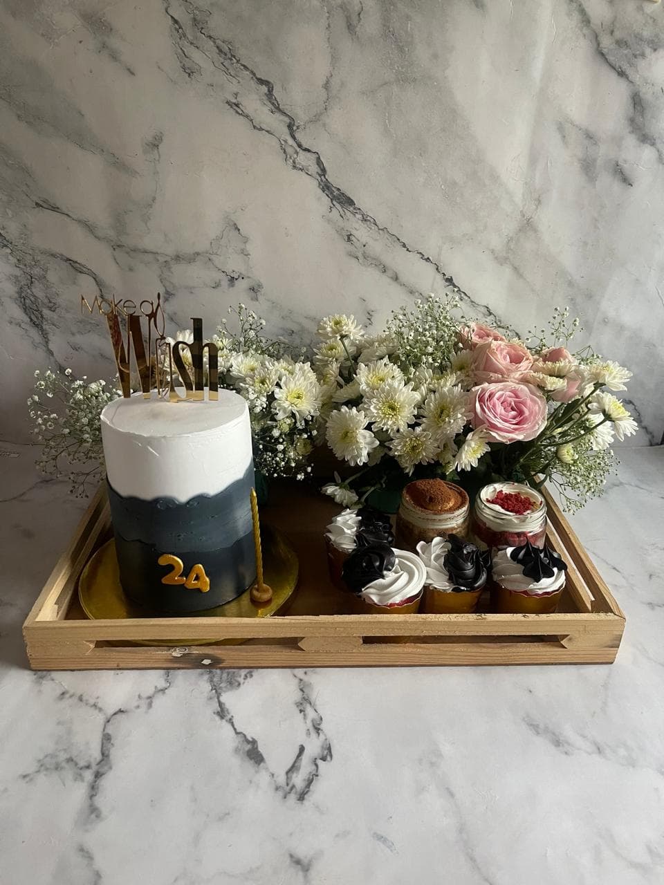 Anniversary dessert tray with a small black cake, flowers, and cupcakes