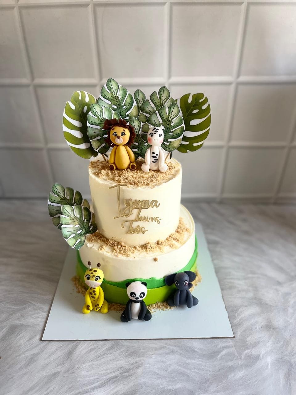 Two-tier jungle animal birthday cake with tropical leaf decorations